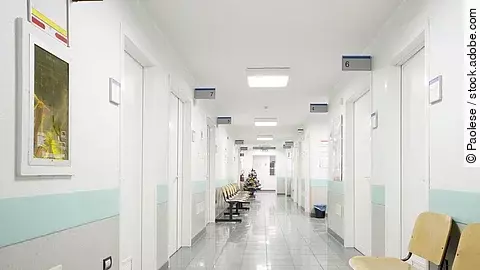 Fotografie eines hellen, weißen Krankenhausflurs mit mehreren Türen und Sitzgelegenheiten.