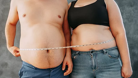 Overweight couple standing together wrapped with measure tape. Dieting, family weight losing and health care concept