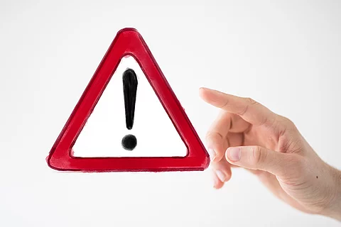 Ein rotes Warnzeichens mit Ausrufezeichen, daneben eine Hand, die darauf zeigt