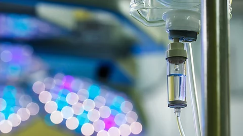 Nahaufnahme einer Infusion im Krankenhaus, unscharfe OP-Lampen im Hintergrund.