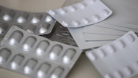 Mehrere silberne Tabletten-Blisterpackungen mit weißen Pillen liegen übereinander auf einer hellen Oberfläche.
