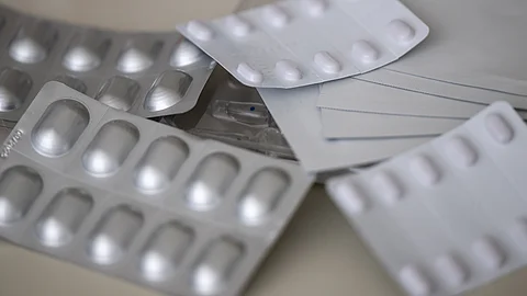 Mehrere silberne Tabletten-Blisterpackungen mit weißen Pillen liegen übereinander auf einer hellen Oberfläche.
