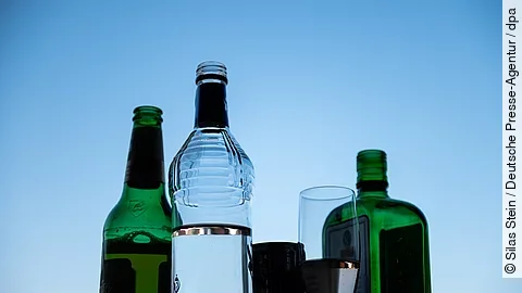Mehrere leere und halbvolle Alkoholflaschen sowie ein Glas vor blauem Himmel