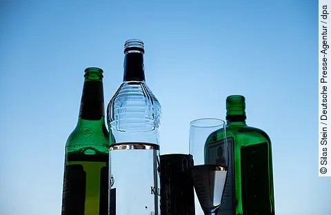 Mehrere leere und halbvolle Alkoholflaschen sowie ein Glas vor blauem Himmel Mehrere leere und halbvolle Alkoholflaschen sowie ein Glas vor blauem Himmel