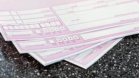 Mehrere rosafarbene ärztliche Rezepte liegen übereinander auf einer dunklen Oberfläche.
