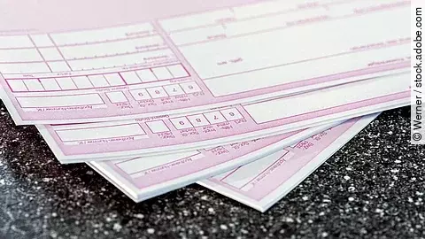 Mehrere rosafarbene ärztliche Rezepte liegen übereinander auf einer dunklen Oberfläche.