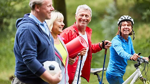 Eine Gruppe erwachsener Menschen ist gemeinsam draußen unterwegs, einige mit Wanderstöcken, eine Person mit Fahrrad; sie bewegen sich in einer grünen, natürlichen Umgebung und wirken aktiv und gut gelaunt. Eine Gruppe erwachsener Menschen ist gemeinsam draußen unterwegs, einige mit Wanderstöcken, eine Person mit Fahrrad; sie bewegen sich in einer grünen, natürlichen Umgebung und wirken aktiv und gut gelaunt.