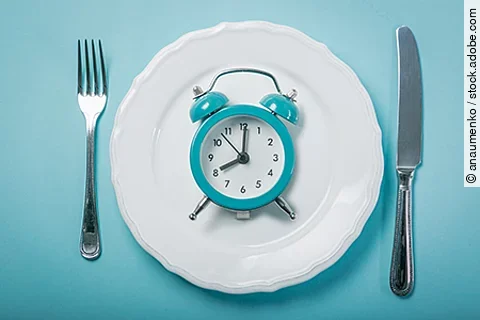 Symbolbild für Fasten: eine analoge Uhr liegt auf einem Teller, daneben liegen Messer und Gabel
