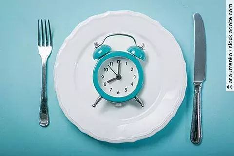Symbolbild für Fasten: eine analoge Uhr liegt auf einem Teller, daneben liegen Messer und Gabel
