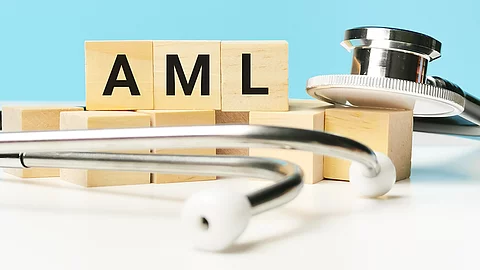 Holzwürfel mit der Aufschrift „AML“ liegen auf einer hellen Fläche, umgeben von einem Stetoskop