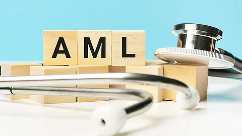 Mehrere Holzklötze mit den Buchstaben „AML“ stehen auf einer Oberfläche; daneben liegt ein Stethoskop vor einem hellblauen Hintergrund.