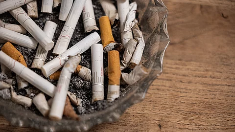 Nahaufnahme eines Glasaschenbechers mit vielen ausgedrückten Zigarettenstummeln auf einer Holzoberfläche
