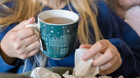Eine Frau trinkt Tee und hält ein Taschentuch in ihrer Hand.