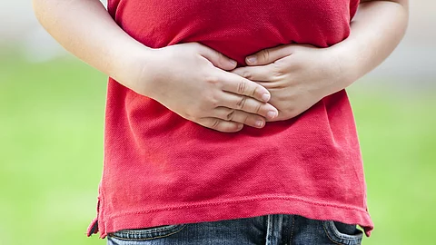 Ein Kind trägt ein rotes T-Shirt und blaue Jeans und hält sich mit beiden Händen den Bauch, was auf Bauchschmerzen hinweist Ein Kind trägt ein rotes T-Shirt und blaue Jeans und hält sich mit beiden Händen den Bauch, was auf Bauchschmerzen hinweist.