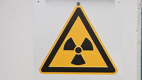 Gelbes dreieckiges Warnschild mit schwarzem Strahlensymbol und der Aufschrift „Radioaktiv“.
