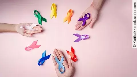 Mehrere Hände halten farbige Schleifen auf rosa Hintergrund, die für unterschiedliche Krebsarten stehen