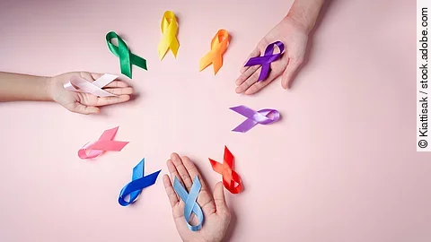 Mehrere Hände halten farbige Schleifen auf rosa Hintergrund, die für unterschiedliche Krebsarten stehen