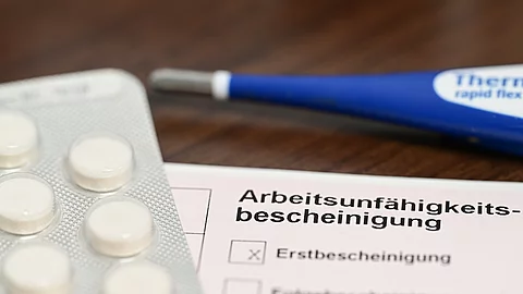 Ein Fieberthermometer, Medikamente und eine ärztliche Arbeitsunfähigkeitsbescheinigung (Krankmeldung) liegen auf einem Nachttisch Ein Fieberthermometer, Medikamente und eine ärztliche Arbeitsunfähigkeitsbescheinigung (Krankmeldung) liegen auf einem Nachttisch