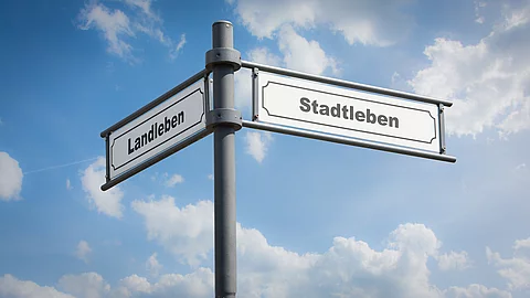 Wegweiser an einem Mast vor blauem Himmel, mit Richtungsangaben für Stadt und Land Wegweiser an einem Mast vor blauem Himmel, mit Richtungsangaben für Stadt und Land