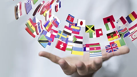 ine ausgestreckte Hand hält zahlreiche kleine Länderflaggen, die halbkreisförmig in der Luft angeordnet sind