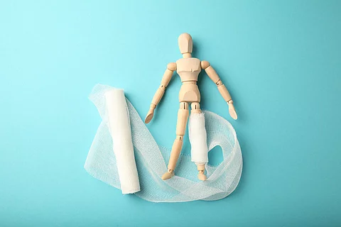 Figure of man with leg wound and white gauze bandage. First aid,