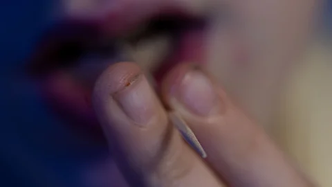 Nahaufnahme einer Hand, die einen dünnen Holz-Zahnstocher zwischen den Fingern hält
