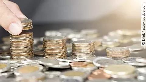 Mehrere Münzstapel, eine Hand legt zusätzliche Münzen darauf.