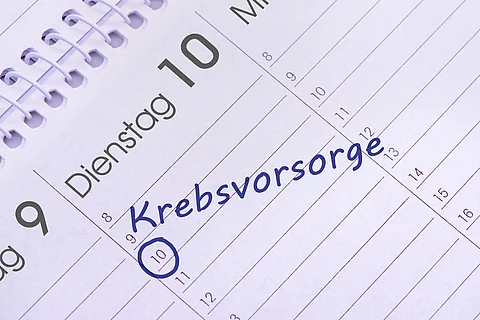 Nahaufnahme eines aufgeschlagenen Kalenders mit handschriftlichem Eintrag ‚Krebsvorsorge‘ am 10. des Monats, blau markiert.