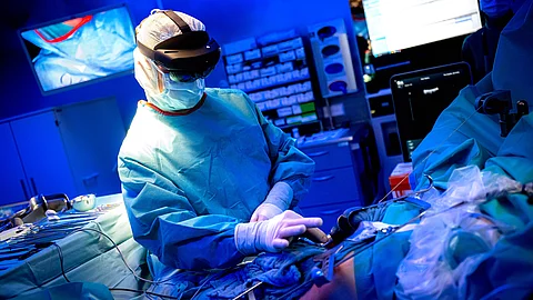 Ein Chirurg steht am OP-Tisch und nutzt eine VR-Brille, um ein virtuelles 3D-Modell der von Krebs befallenen Leber des Patienten in sein Sichtfeld einzublenden. 