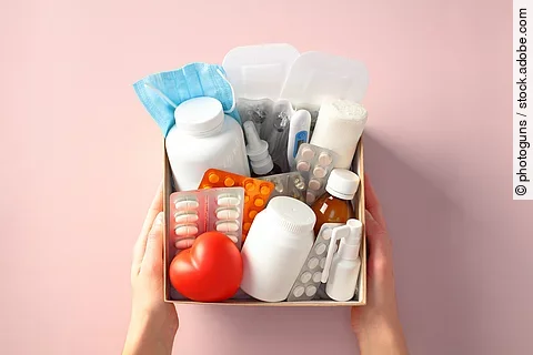 Box with essential healthcare kit with medication, pills, bandages, and face mask in female hands. Medical donations, first aid kit, home delivery of medications, online pharmacy concept.