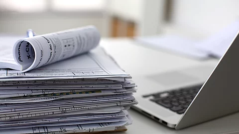 Dokumentenstapel und Laptop als Symbol der Überbelastung von Ärzten und Pflegekräften