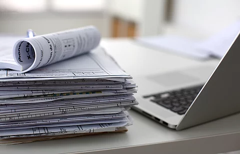 Dokumentenstapel und Laptop als Symbol der Überbelastung von Ärzten und Pflegekräften