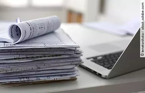 Dokumentenstapel und Laptop als Symbol der Überbelastung von Ärzten und Pflegekräften