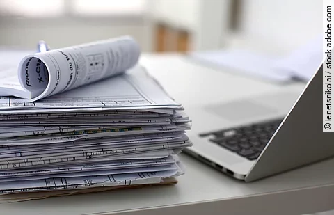 Dokumentenstapel und Laptop als Symbol der Überbelastung von Ärzten und Pflegekräften
