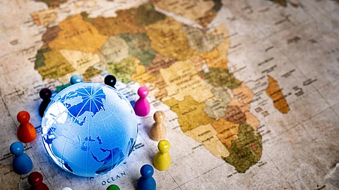 Ein Globus liegt auf einer Weltkarte, zu sehen ist der afrikanische Kontinent, umgeben von verschiedenfarbigen Spielfiguren,
