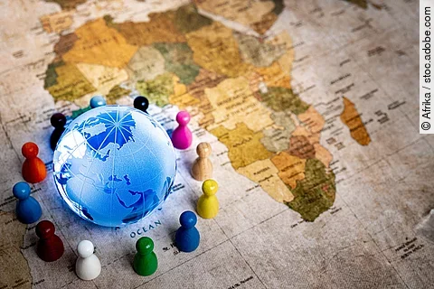 Ein Globus liegt auf einer Weltkarte, zu sehen ist der afrikanische Kontinent, umgeben von verschiedenfarbigen Spielfiguren,