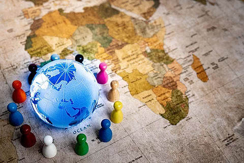 Ein Globus liegt auf einer Weltkarte, zu sehen ist der afrikanische Kontinent, umgeben von verschiedenfarbigen Spielfiguren,